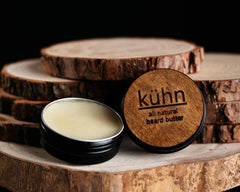 A 2oz tin Beard Butter in front of some wood cookies showing the inside and wooden label.